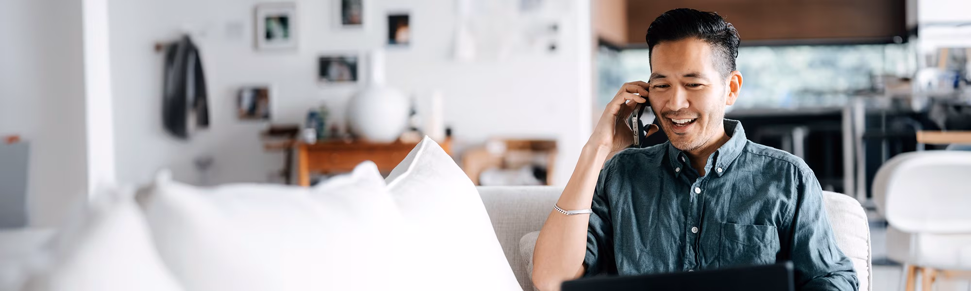 A middle-aged man smiles while talking on his mobile phone in a modern white living room.