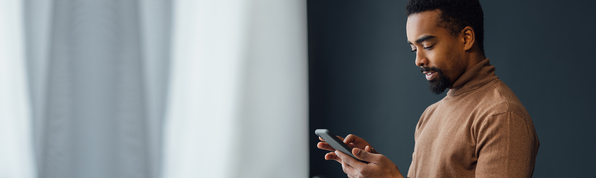 Man using a phone next to a curtained window